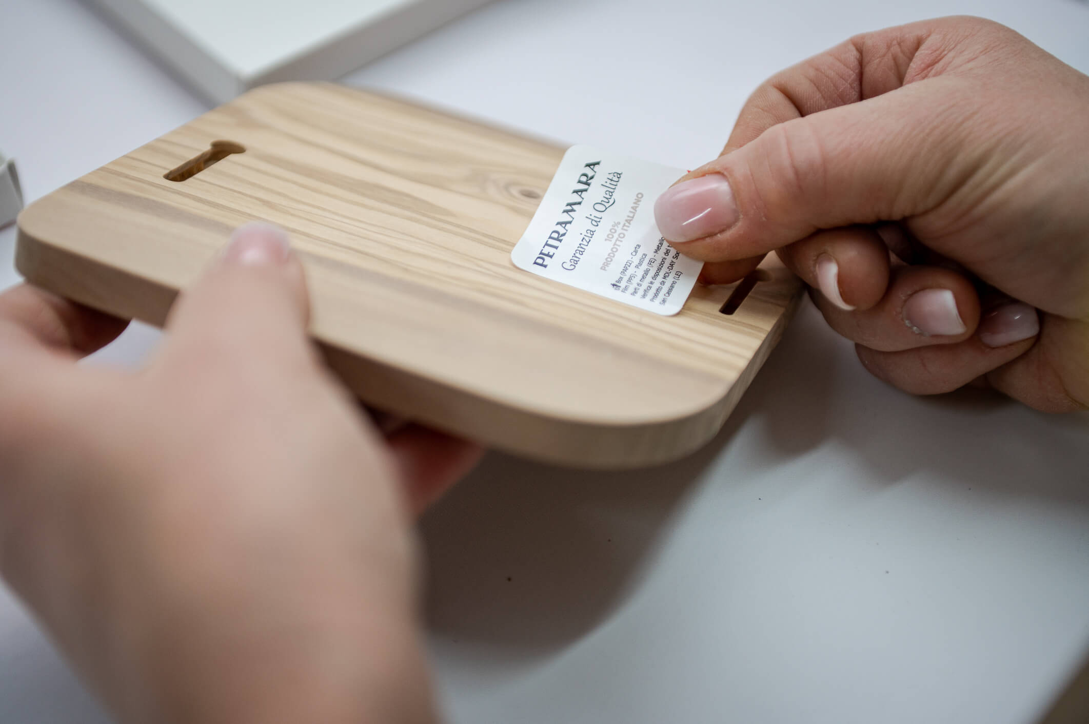 Applicazione dell’etichetta “Garanzia di Qualità” sul retro di un prodotto in legno di ulivo levigato e con venature naturali.