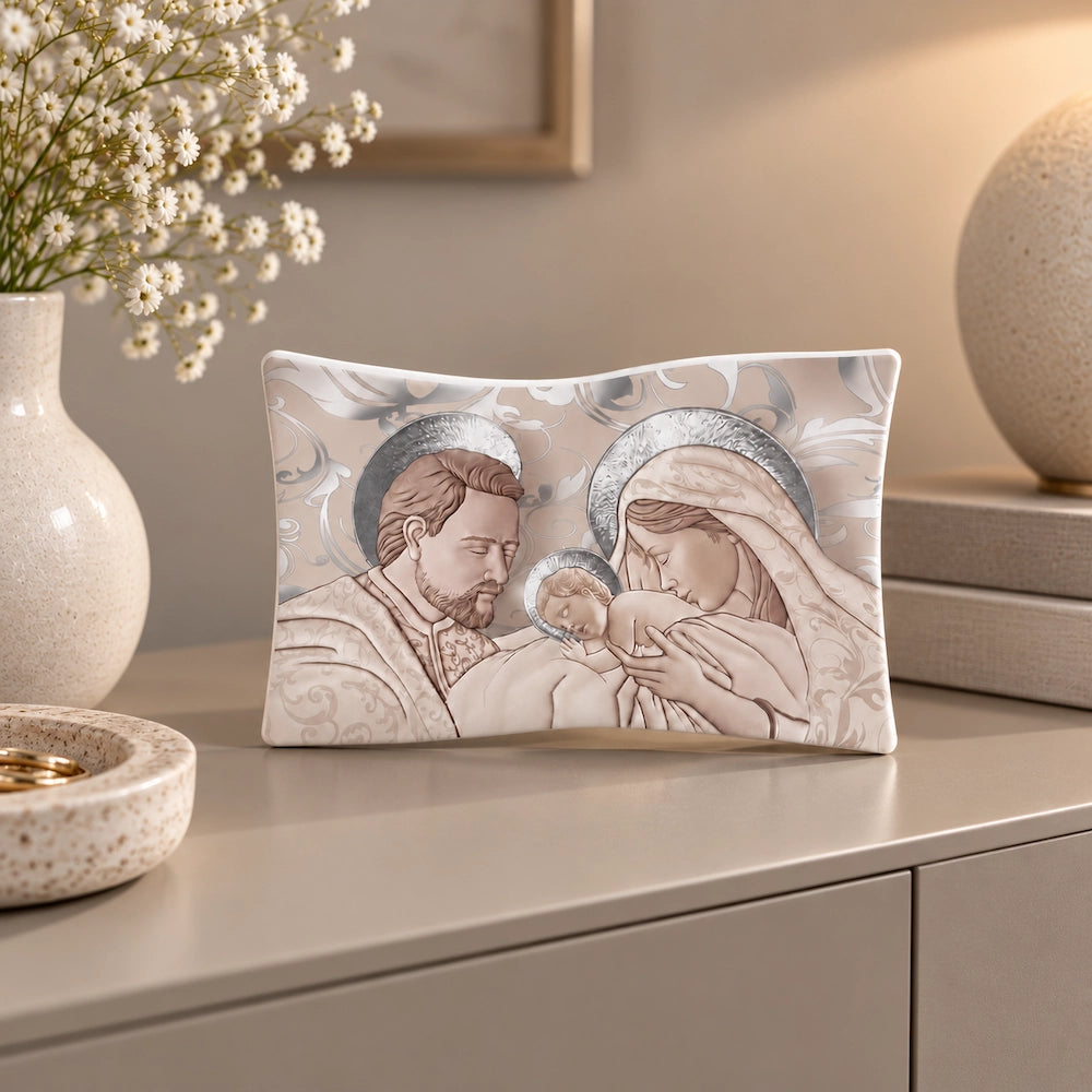 Bomboniera Sacra Famiglia in tonalità beige e tortora, ambientata su mobile moderno laccato opaco con fiori bianchi e dettagli decorativi neutri.