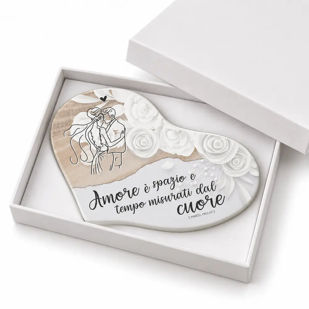 Bomboniera matrimonio a forma di cuore con coppia di sposi, fiori bianchi e frase sull’amore, inserita in scatola regalo bianca.