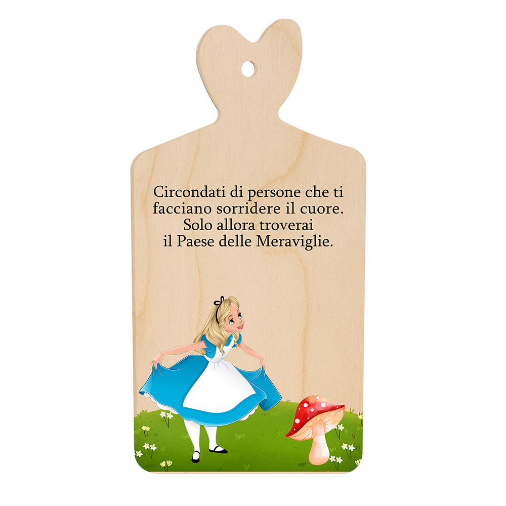 Tagliere in legno a forma di cuore con frase incisa e illustrazione di una bambina accanto a un fungo su prato verde.