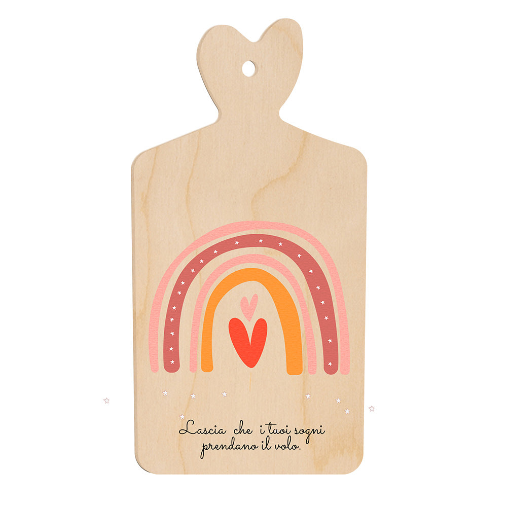 Tagliere in legno a forma di cuore con arcobaleno stilizzato nei toni rosa e arancio e frase “Lascia che i tuoi sogni prendano il volo” nella parte inferiore.