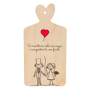 Tagliere in legno a forma di cuore con frase romantica e illustrazione stilizzata di sposi che si tengono per mano sotto un palloncino rosso a forma di cuore.