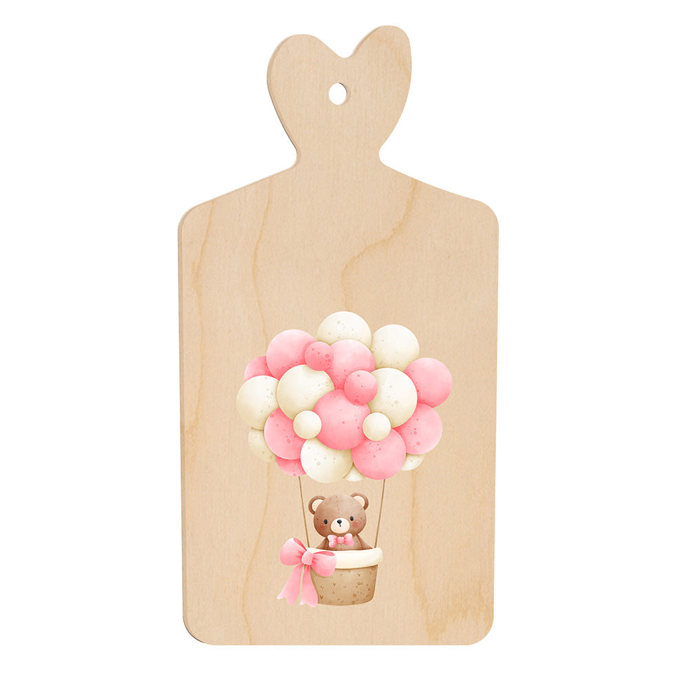 Tagliere in legno a forma di cuore con illustrazione di un orsetto in mongolfiera fatta di palloncini rosa e bianchi, in stile dolce e infantile.