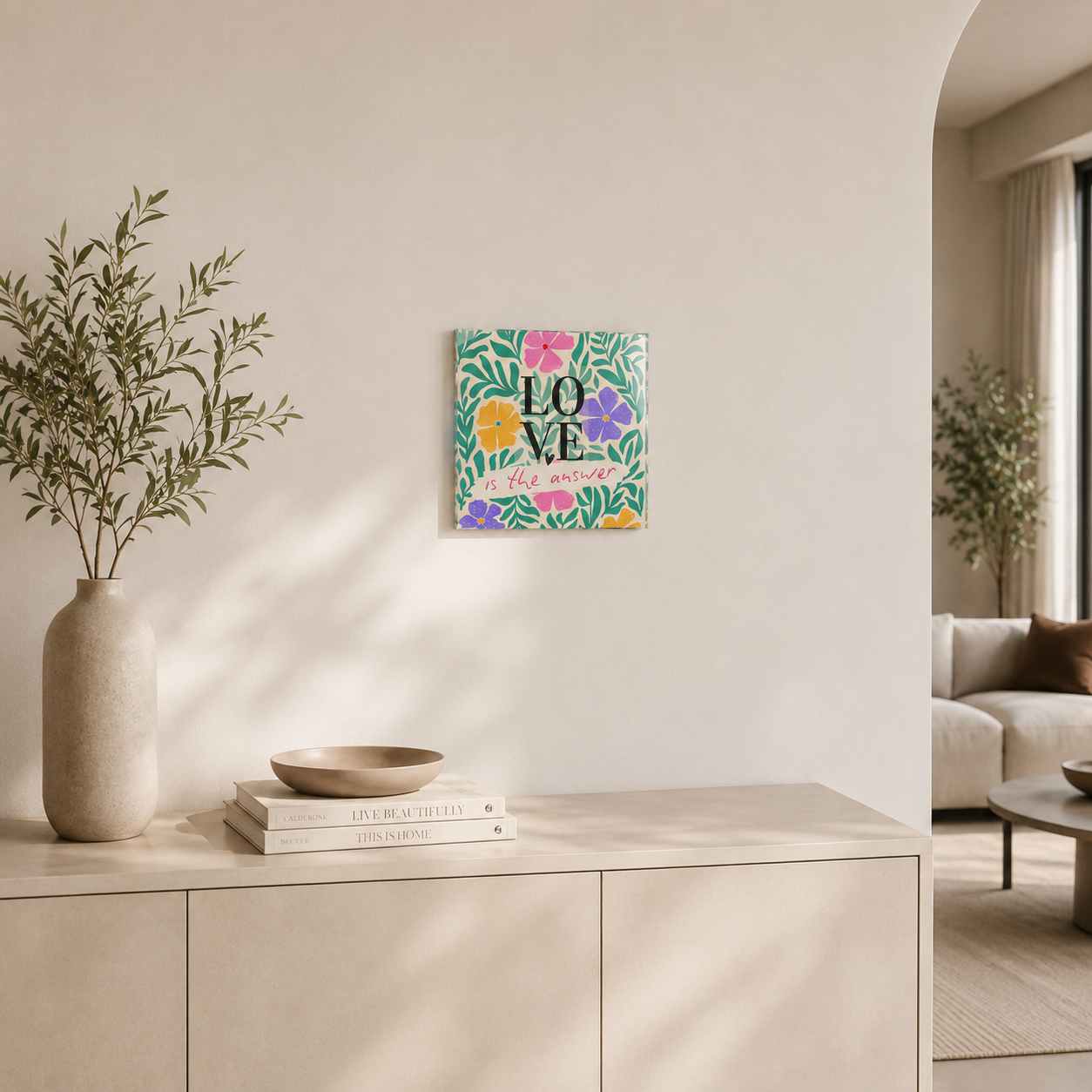 Quadro in vetro 30x30 cm con scritta “Love is the answer”, ambientato in un soggiorno moderno e minimalista dai toni neutri.
