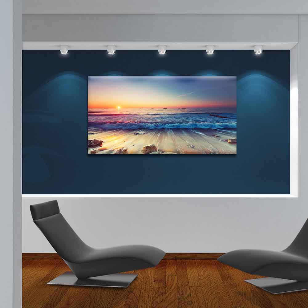 Quadro in plexiglass o vetro con scenario marino al crepuscolo, appeso su parete blu in soggiorno moderno con sedute minimal.