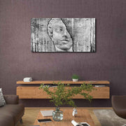 Quadro in plexiglass o vetro con immagine di testa scolpita su fondo grezzo, appeso in salotto con arredi naturali e toni caldi.