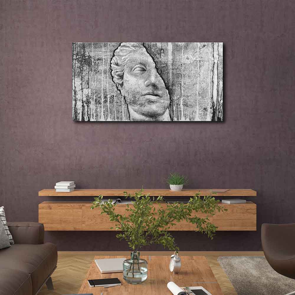 Quadro in plexiglass o vetro con immagine di testa scolpita su fondo grezzo, appeso in salotto con arredi naturali e toni caldi.