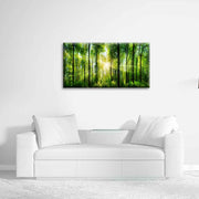 Quadro in plexiglass o vetro con foresta verde illuminata dal sole, appeso su parete bianca in soggiorno con divano moderno total white.