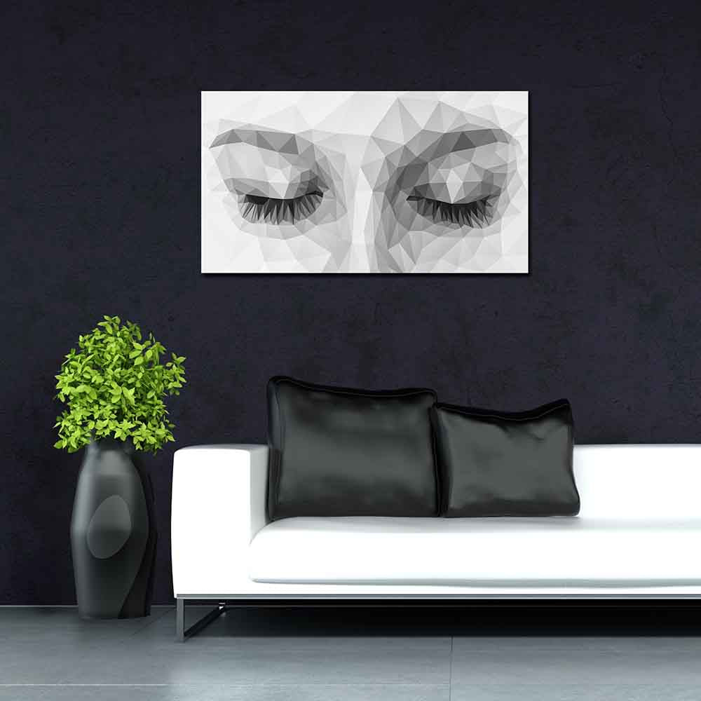 Quadro in plexiglass o vetro con volto composto da triangoli monocromatici, montato su parete scura sopra divano bianco con cuscini neri.