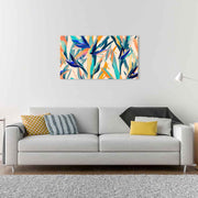 Quadro in plexiglass o vetro con fiori di strelitzia colorati, posizionato sopra un divano per un tocco tropicale ed elegante.