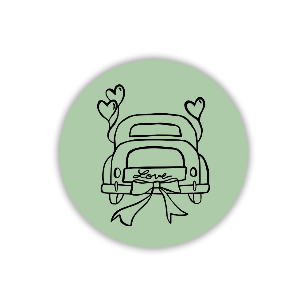 Magnete circolare in legno verde salvia con disegno nero di auto nuziale, cuori e targa Love. Idea segnaposto per nozze ecosostenibili.