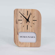 Orologio portafoto in ulivo con cornice per foto integrata, posizionato su un tavolo, evidenziando le venature naturali del legno.