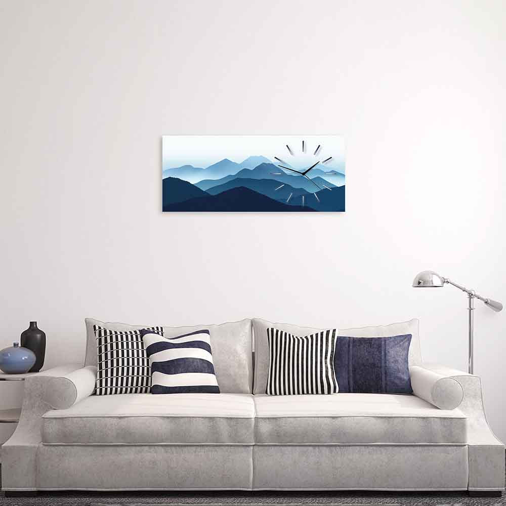 Orologio in plexiglass con decorazione di montagne blu avvolte nella nebbia, posizionato sopra un divano in un ambiente moderno.