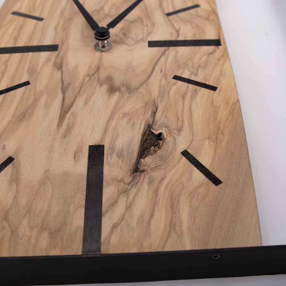 Dettaglio dell'orologio ulivo acciaio da parete, primo piano sulla texture del legno e il raffinato bordo in acciaio.