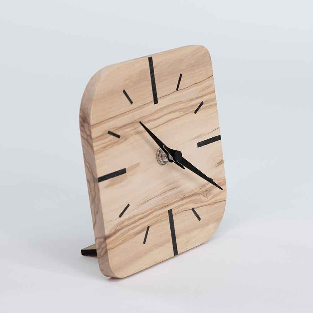 Vista laterale di un piccolo orologio in ulivo da tavolo, evidenziando la compattezza e la finitura levigata del legno naturale.