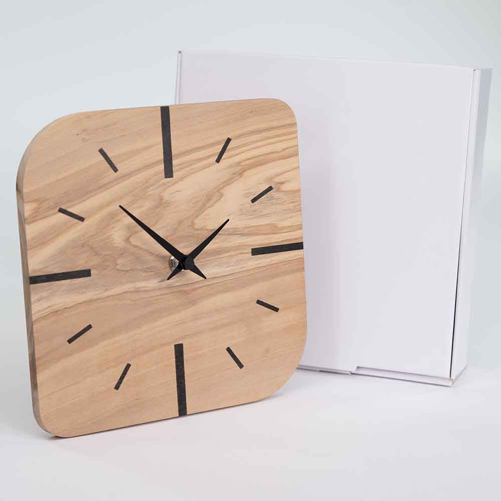 Orologio in ulivo da tavolo quadrato vicino alla sua confezione elegante, allineato perfettamente per mostrare il design essenziale e naturale.