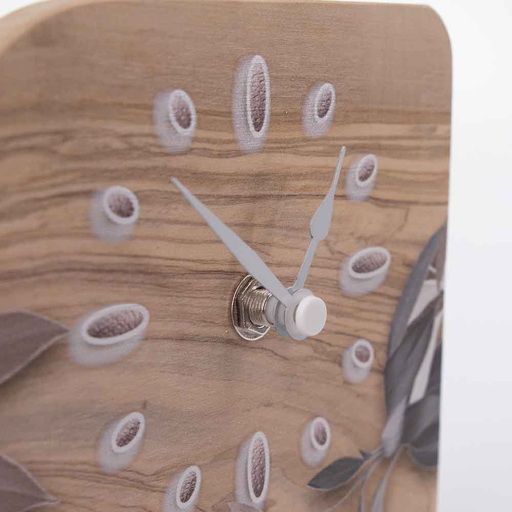 Dettaglio delle lancette di un orologio in ulivo da tavolo con decoro a foglie, evidenziando il contrasto tra design e funzionalità.