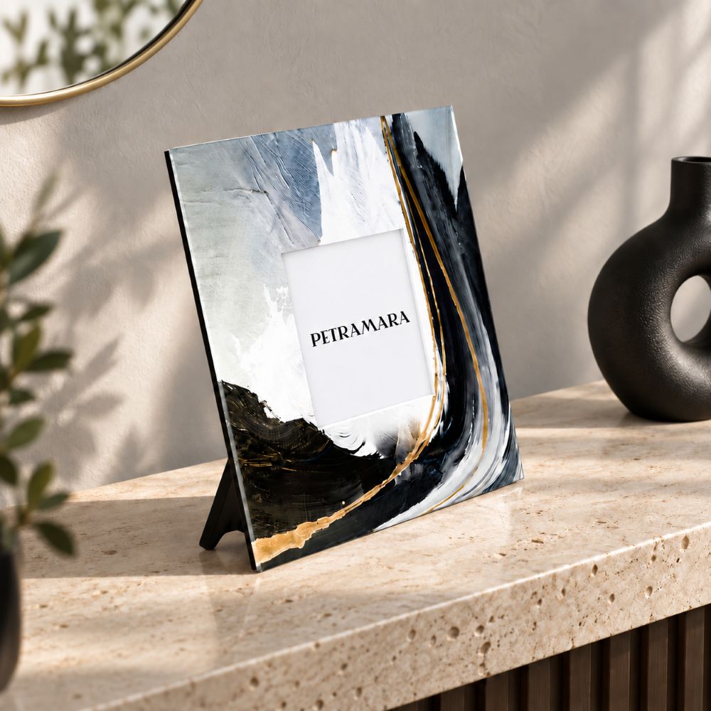 Portafoto quadrato in vetro Black Wave con pennellate nere, bianche e dorate, ambientato su una consolle in travertino moderna