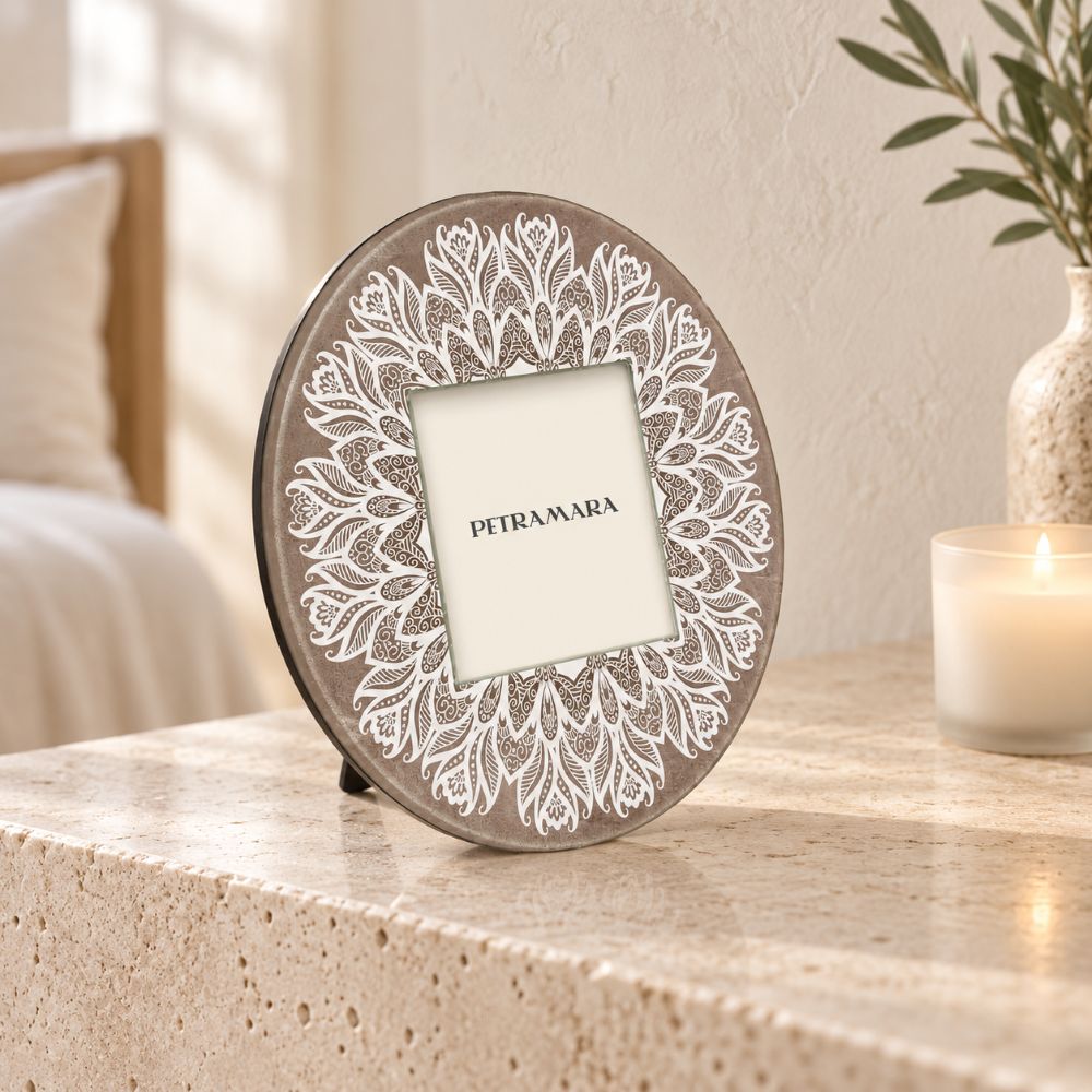 Portafoto rotondo in vetro Mandala con decoro bianco su fondo tortora, ambientato su una consolle in travertino in una camera luminosa