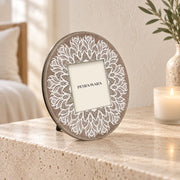 Portafoto rotondo in vetro Mandala con decoro bianco su fondo tortora, ambientato su una consolle in travertino in una camera luminosa