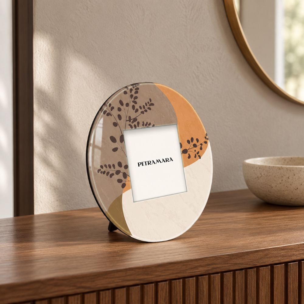 Portafoto rotondo in vetro Twigs con decoro botanico nei toni beige e terracotta, ambientato su una consolle in legno moderna