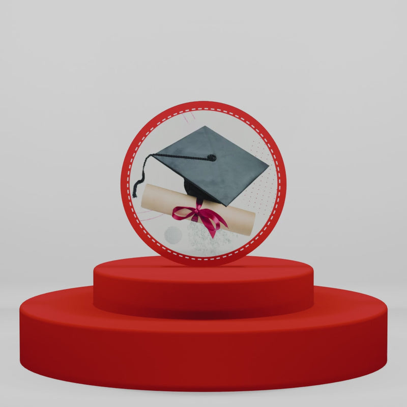 Magnete tondo in legno per laurea con tocco nero e diploma con nastro rosso. Idea regalo o bomboniera celebrativa su piedistallo rosso intenso.