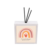 Profumatore ambiente ceramica bianco con arco arcobaleno in fasce rosa e arancio, cuore rosso e scritta ispirazionale su sfondo crema, reed neri