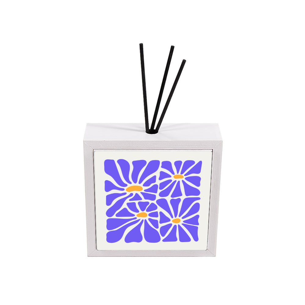 Profumatore ceramica bianco con piastrella floreale, quattro grandi margherite in blu pervinca e centri arancio su sfondo bianco, bastoncini reed neri