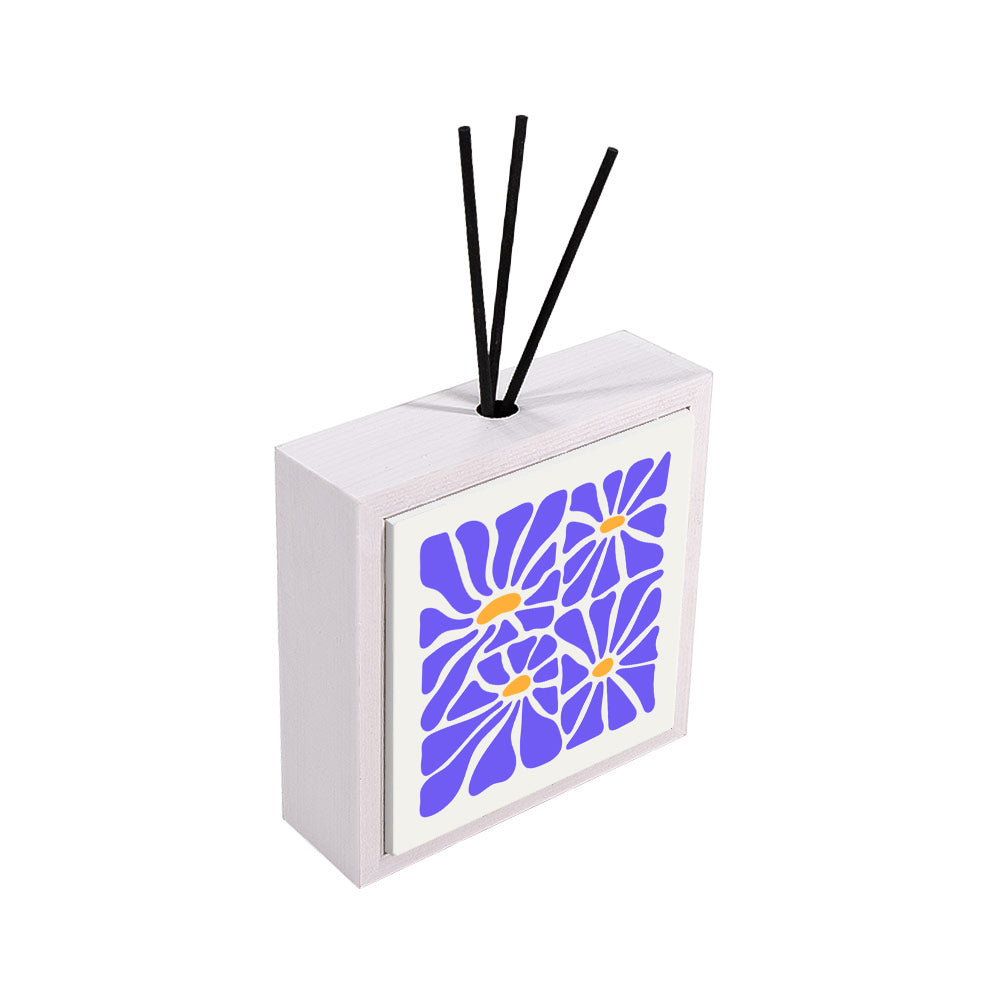 Modello profumatore ceramica bianco vista laterale, piastrella con 4 margherite in blu pervinca e centri arancio su sfondo bianco, bastoncini reed neri