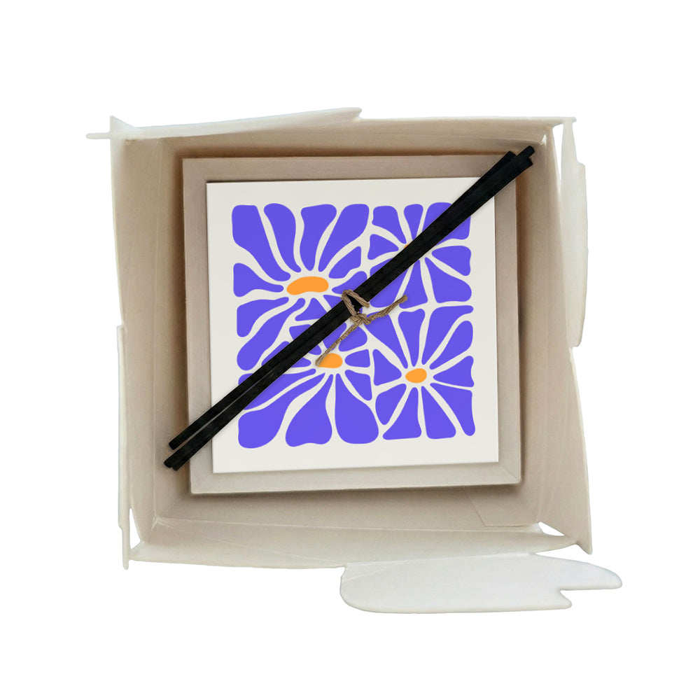 Profumatore ceramica in scatola, piastrella con quattro margherite blu pervinca e centri arancio su sfondo bianco, bastoncini reed neri in confezione