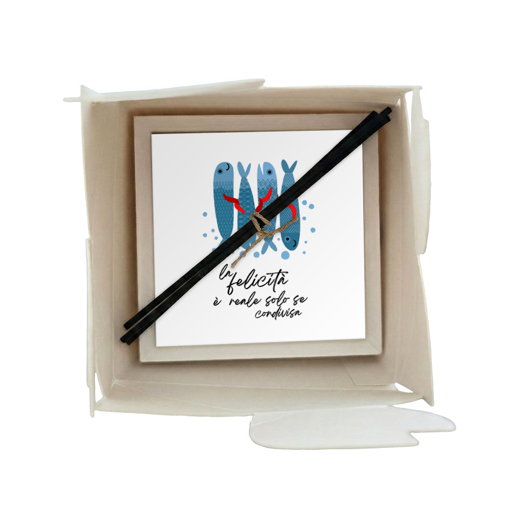 Profumatore ceramica in scatola pesci blu con accenti rossi e scritta "la felicità è reale solo se condivisa", sfondo bianco, bastoncini reed neri