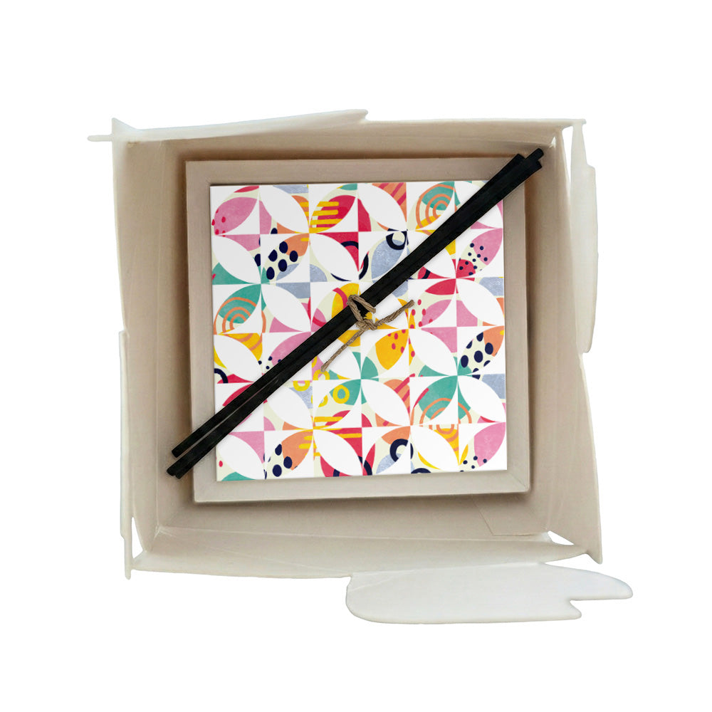 Profumatore ceramica in scatola con piastrelle geometriche multicolore, forme a petalo in rosa, turchese, giallo e blu navy su sfondo bianco, bastoncini reed neri
