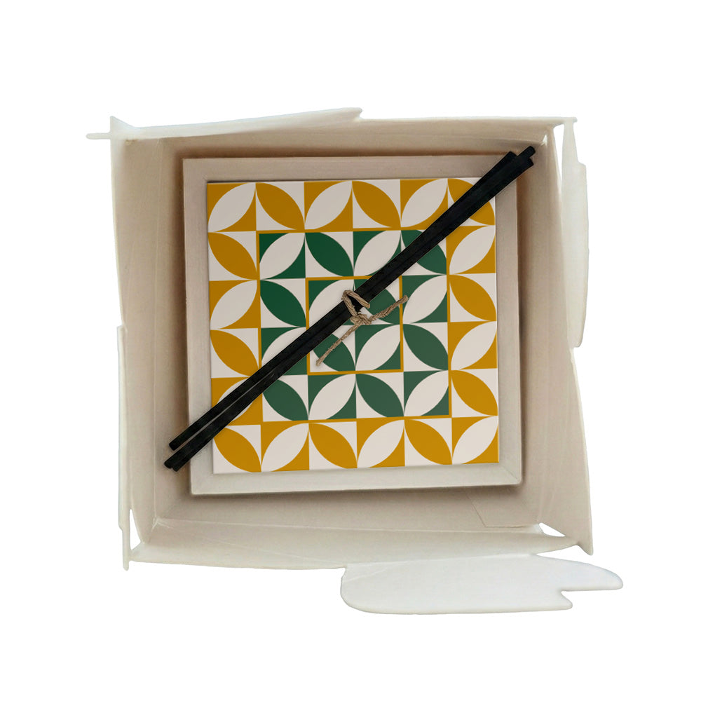 Profumatore ceramica in scatola con motivo geometrico a piastrella in giallo ocra e verde scuro, forme a petalo ripetute su sfondo bianco, bastoncini reed neri