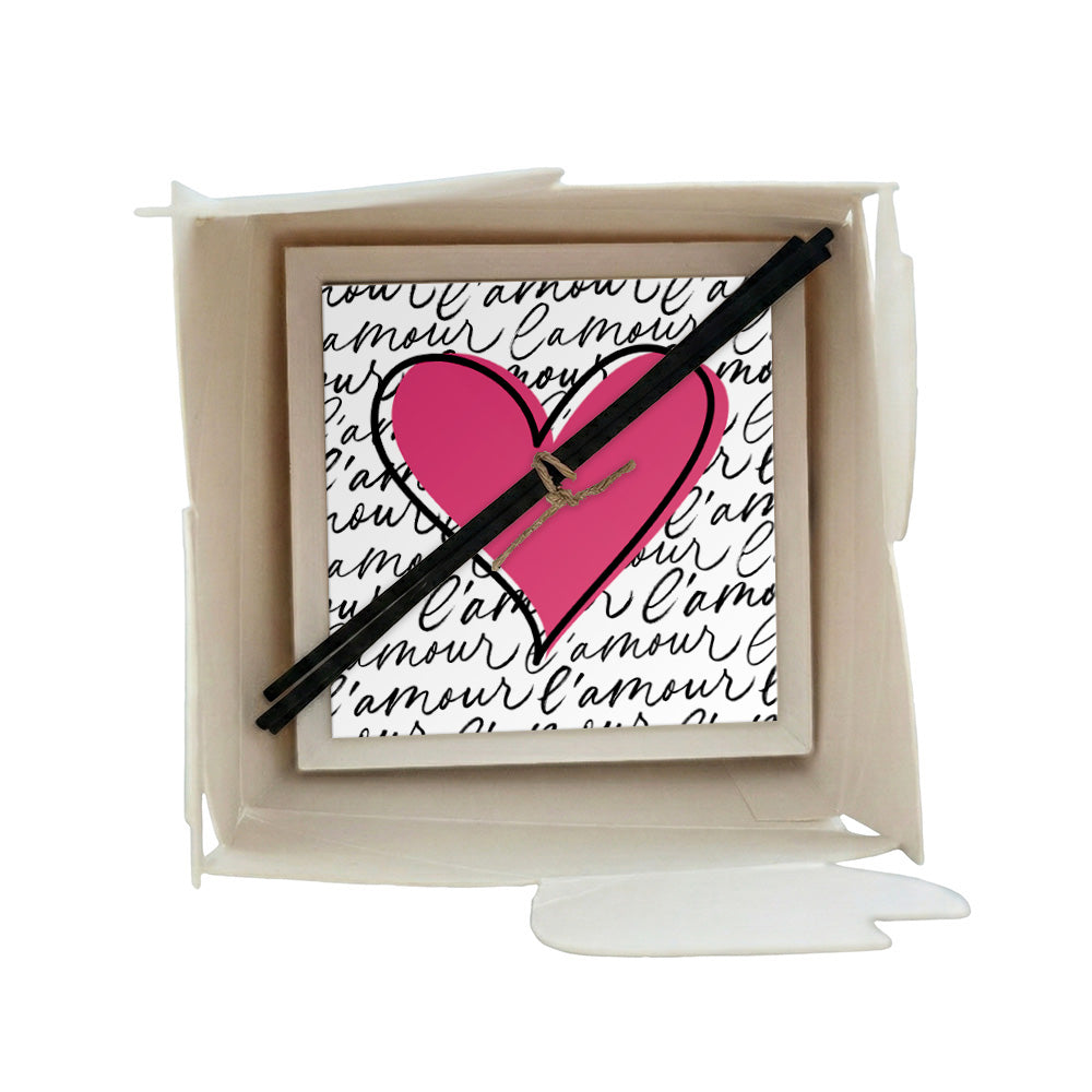 Profumatore ceramica con cuore rosa fucsia e scritta "l'amour" ripetuta in corsivo su sfondo bianco, design romantico, bastoncini reed neri in confezione