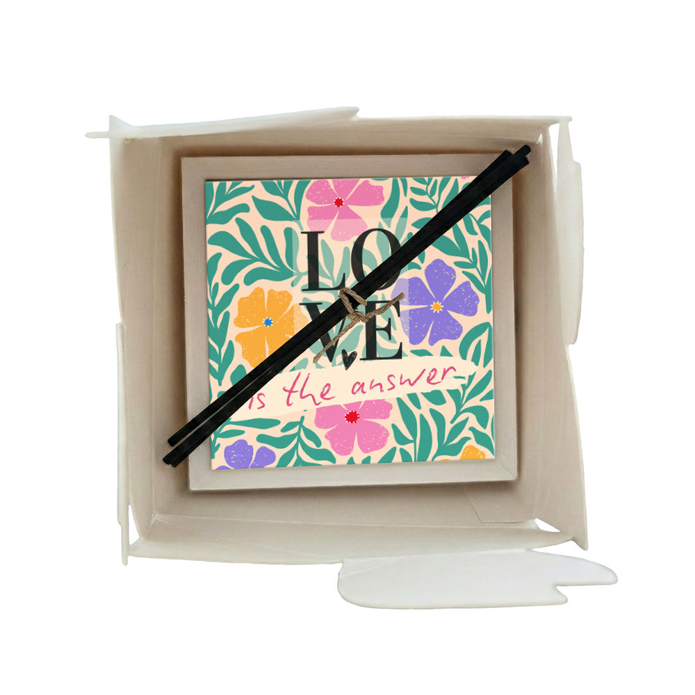 Profumatore ceramica in scatola con fiori tropicali rosa, viola e arancio, foglie verdi e scritta "LOVE is the answer" su sfondo pesca, bastoncini reed neri