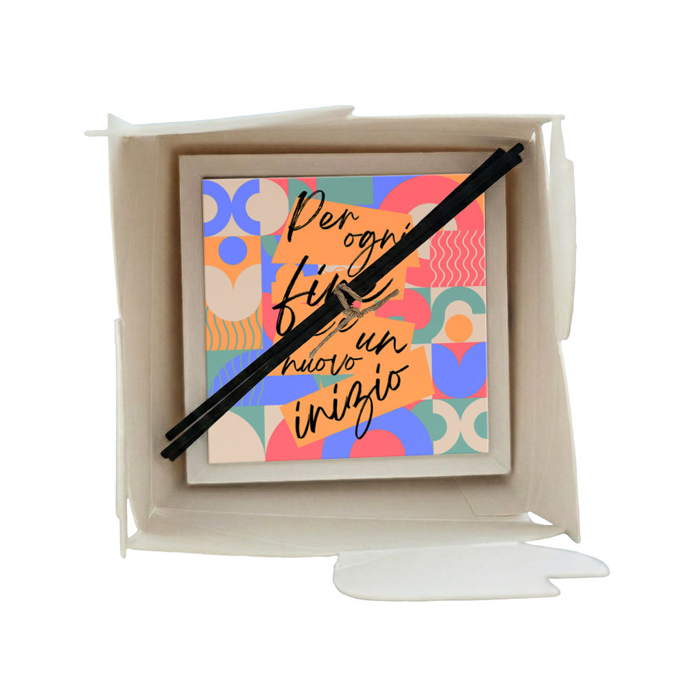 Profumatore ceramica in scatola con forme geometriche astratte in arancio, blu, rosa e turchese e scritta "Per ogni fine c'è un nuovo inizio", bastoncini reed neri