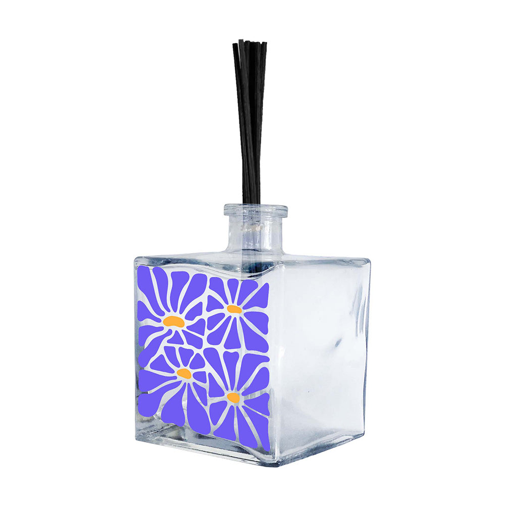 Profumatore ambiente in vetro trasparente quadrato, decoro con quattro margherite in blu pervinca e centri arancio su sfondo bianco, bastoncini reed neri
