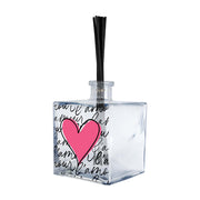 Profumatore ambiente vetro trasparente quadrato, decoro con grande cuore rosa fucsia e scritta "l'amour" ripetuta in corsivo nero, bastoncini reed neri