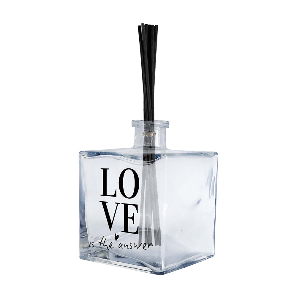 Profumatore ambiente vetro quadrato, etichetta minimal con scritta LOVE in caratteri bold neri e frase "is the answer" in corsivo con cuore, reed neri