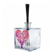 Profumatore ambiente in vetro quadrato, decorato con albero chioma a cuore con foglie rosse, fucsia, viola su rami viola intrecciati, sfondo bianco, reed neri
