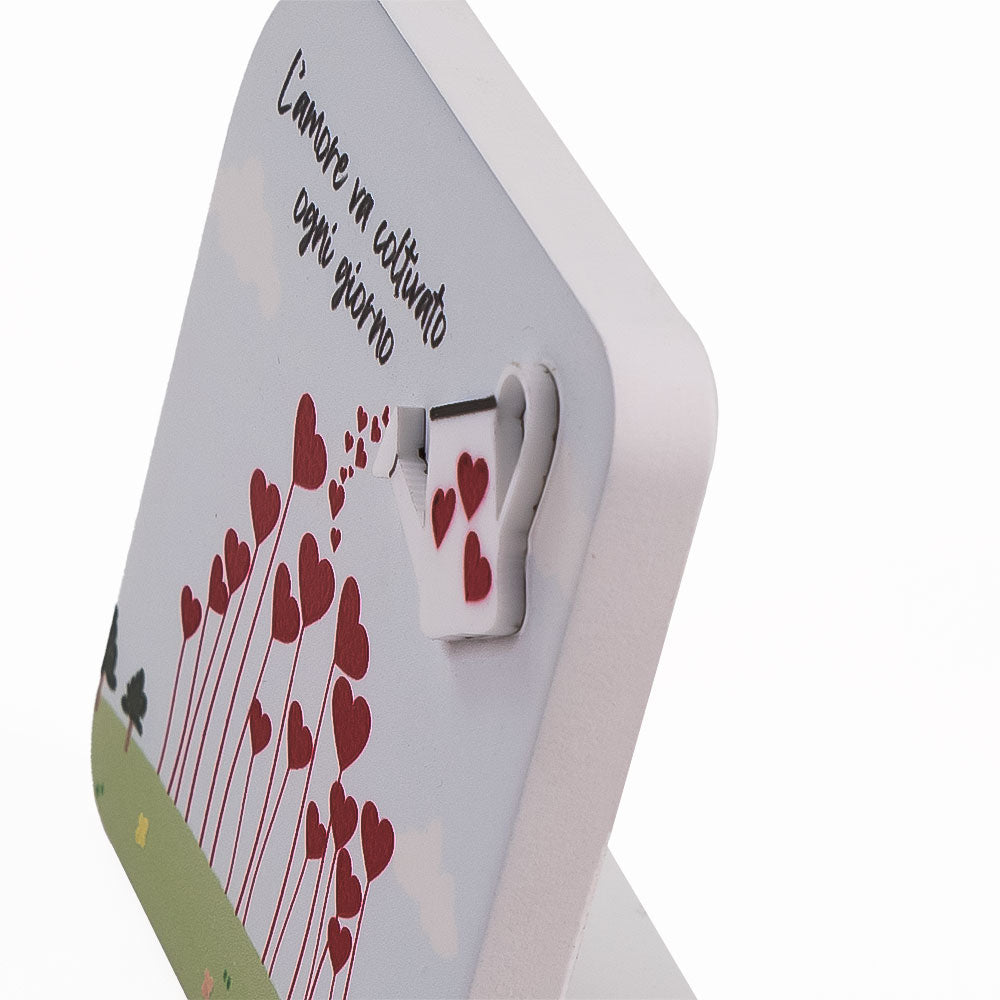 Vista ravvicinata del quadretto in legno con annaffiatoio e cuori in rilievo, che crea un effetto tridimensionale su sfondo decorato.