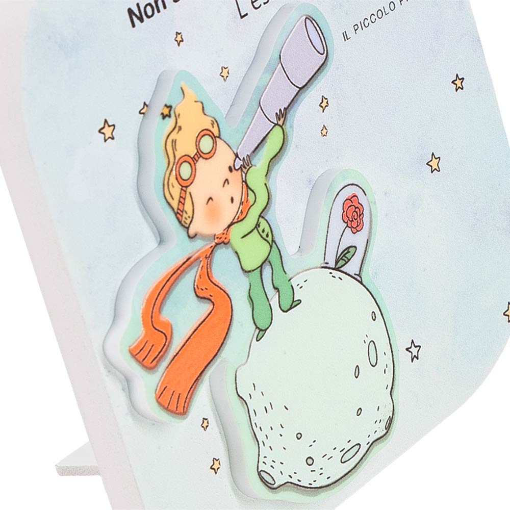 Dettaglio del quadretto in legno con il Piccolo Principe in rilievo e telescopio, evidenzia profondità e texture su base decorata con stelle.