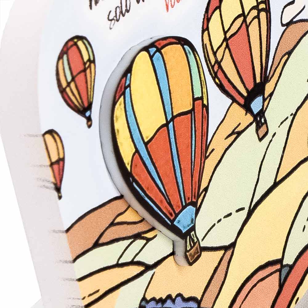 Dettaglio ravvicinato di quadretto in legno con mongolfiera multicolore in rilievo su sfondo collinare, mostra spessore e colori accesi.