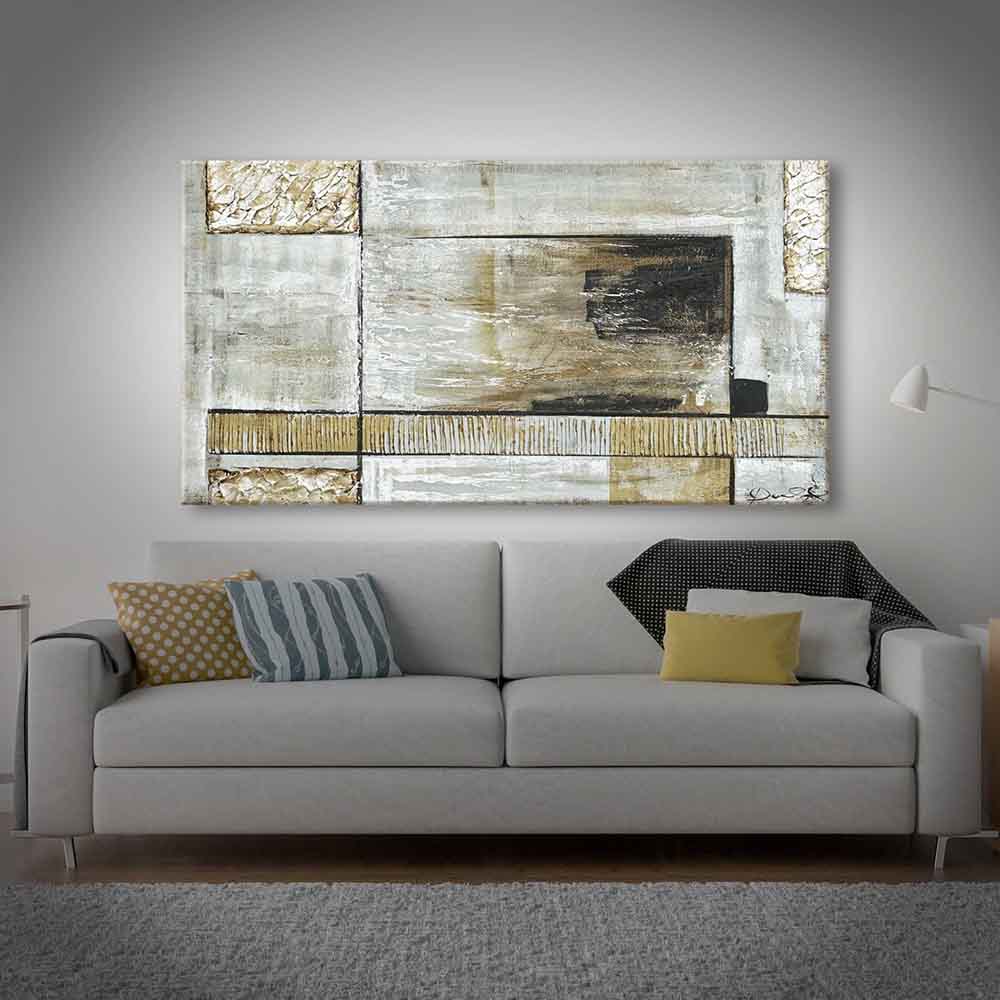 Quadro dipinto a mano con motivi geometrici con tonalità calde e neutre, appeso sopra un elegante divano grigio in un salotto moderno.