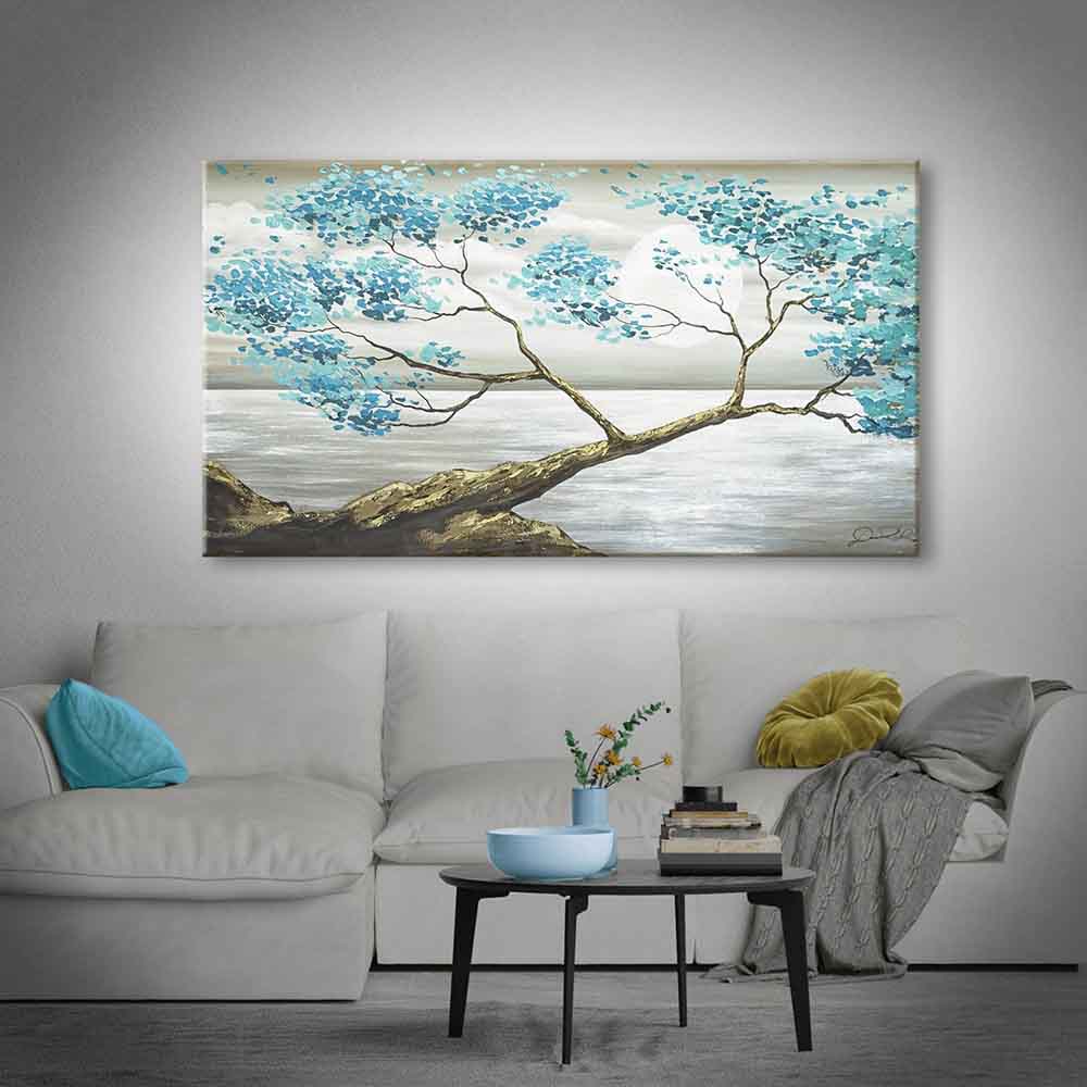 Quadro dipinto a mano con albero dai fiori azzurri, posizionato sopra un elegante divano chiaro in un soggiorno moderno e accogliente.