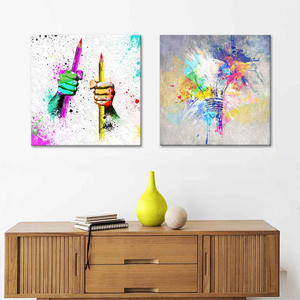 Due quadri astratti su tela sopra una credenza in legno: mani colorate con matite e lampadina con esplosione di colori, simbolo di creatività.