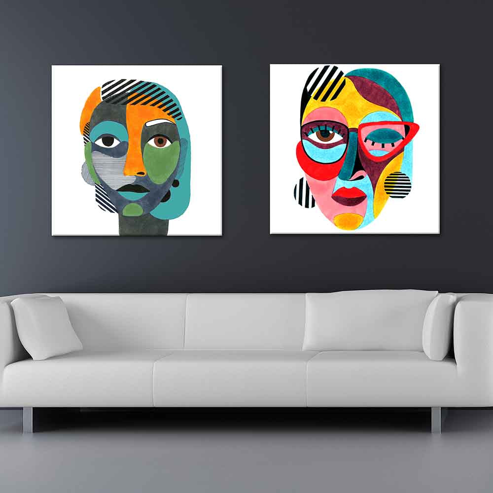 Coppia di quadri su tela con ritratti femminili astratti in stile pop, con forme colorate e motivi a righe su sfondo bianco, sopra divano grigio.