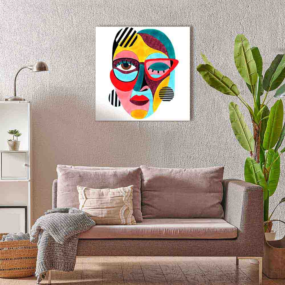 Quadro su tela con volto astratto dai colori vivaci e occhiali rossi, esposto in un soggiorno con divano grigio e cuscini arcobaleno.