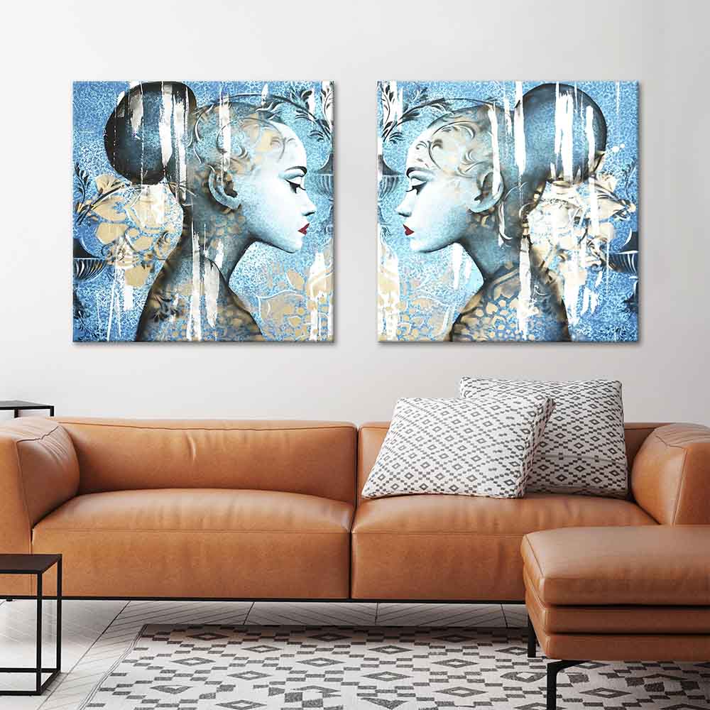 Coppia di quadri con figure femminili opposte su sfondo azzurro damascato, sopra divano in pelle color cuoio.