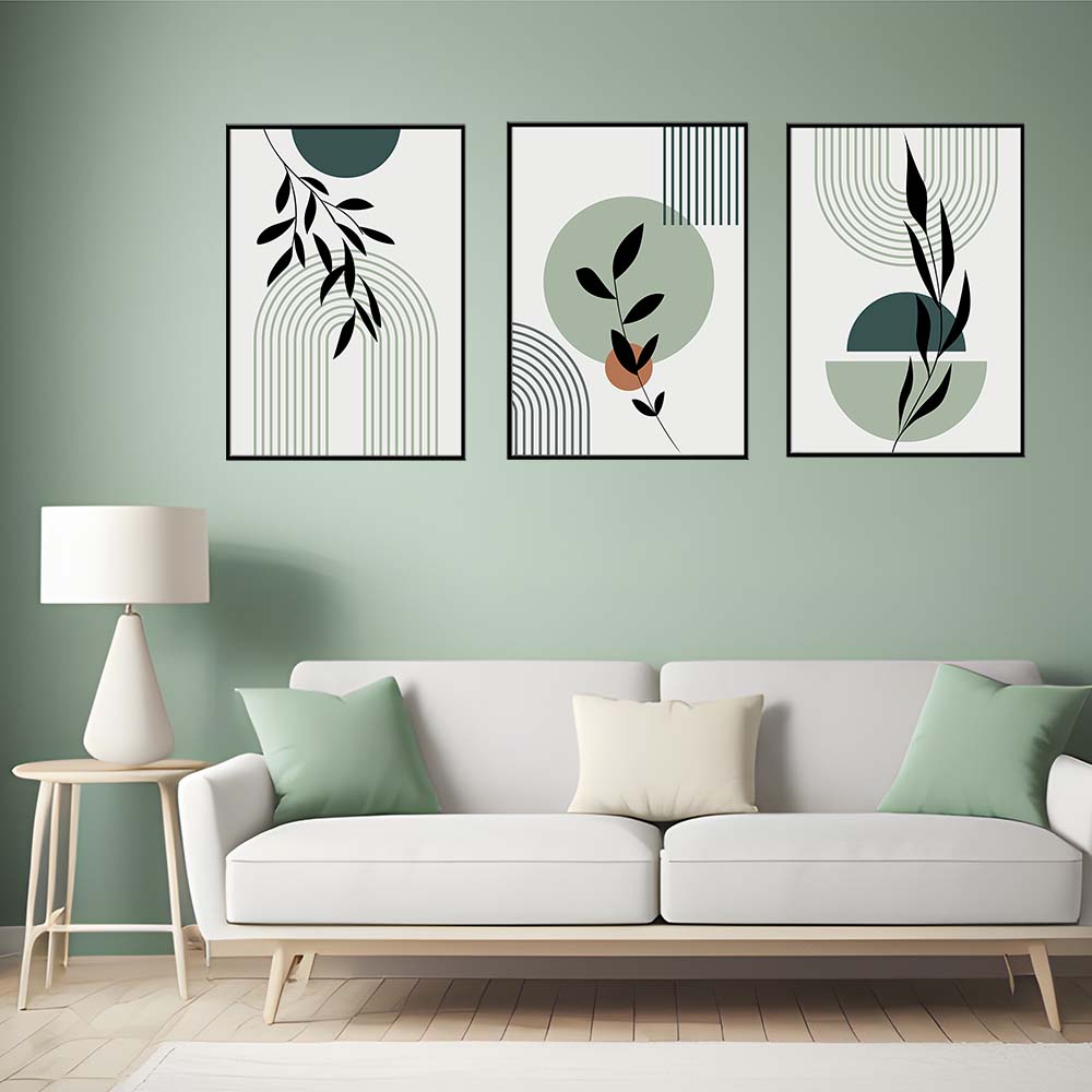 Tris di quadri appesi in fila sopra un divano chiaro: linee ad arco verde salvia, cerchi verde petrolio e rami neri.